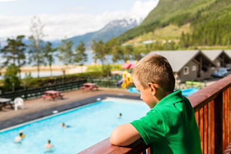 Young boy overlooking the swimming pool area at summer holiday resort at Kinsarvik near Hardangerfjord in Norway.の写真素材