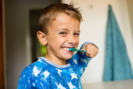 Close-up of young boy brushing his teeth with toothbrush while standing in bathroom with natural...