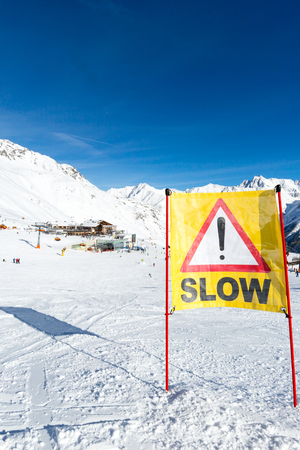 Yellow slow down warning sign placed in the snow on the piste at the ski resort Soelden in Austria.の写真素材