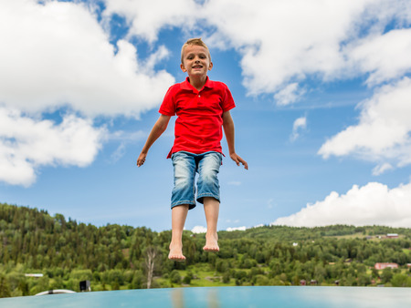 Young Scandinavian boy playing and having fun while jumping up and down on inflatable bouncing trampoline.の写真素材