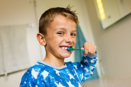 Close-up of young boy brushing his teeth with toothbrush while standing in bathroom with natural...