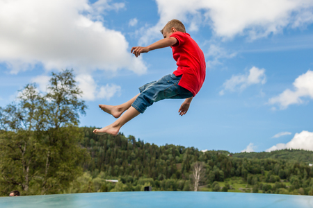 Young Scandinavian boy playing and having fun while jumping up and down on inflatable bouncing pillow.の写真素材
