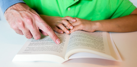 Close-up of young boy reading a text book while sitting at white table.