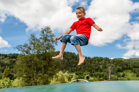 Young Scandinavian kid playing and having fun while jumping up and down on inflatable bouncing trampoline.の写真素材