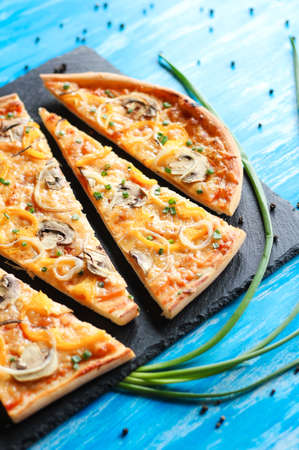 Slised vegeterian home made pizza with yellow pepper and mushrooms, onion, tomatoes on blue tableの写真素材