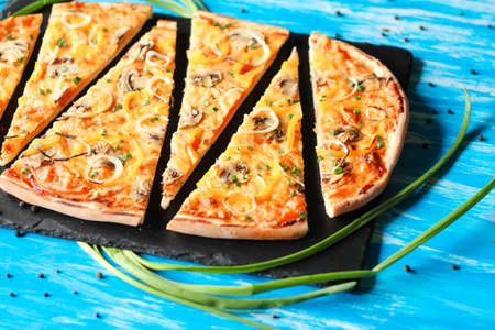 Slised vegeterian home made pizza with yellow pepper and mushrooms, onion, tomatoes on blue tableの写真素材