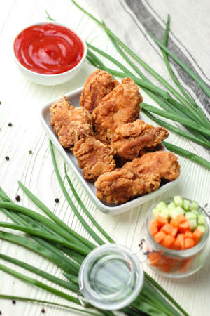 Chicken wings in breading with sliced vegetables and tomato sauce on white wooden tableの写真素材