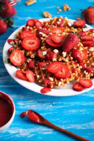 Waffles with strawberry and nuts on white plate on blue background.の写真素材