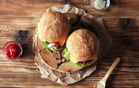 Two handmade burgers with beef, salad and cheese on wooden brown table. Buns with sesame seedsの写真素材