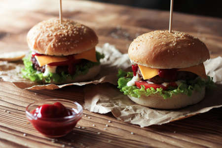 Two handmade burgers with beef, salad and cheese on wooden brown table. Buns with sesame seedsの写真素材