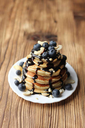 Stack of pancakes with blueberries and chocolate sauce on wooden background. Rustic style