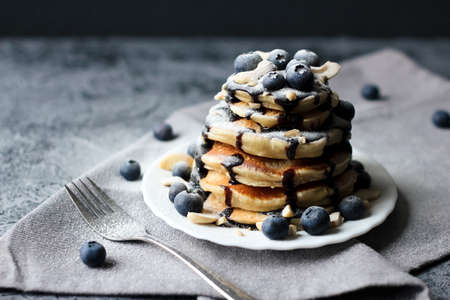 Stack of pancakes with blueberries and chocolate sauce on a gray concrete background. Rustic style