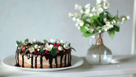 Drip cake with chocolate, decorated with strawberries, jasmine flowers and honeysuckle on white...