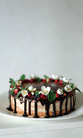Drip cake with chocolate, decorated with strawberries, jasmine flowers and honeysuckle on white...