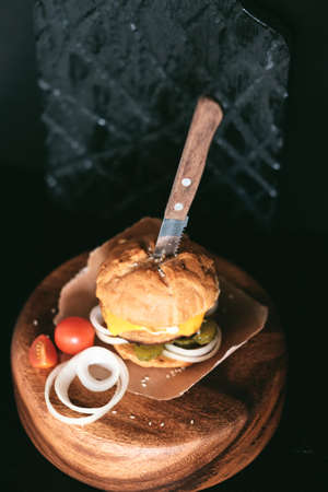 Handmade burger with beef, pickles, cheese, onion and knife on wooden table.の写真素材