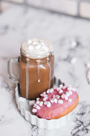 Pink donut with marshmallow and hot chocolate in glass cup on table.の写真素材