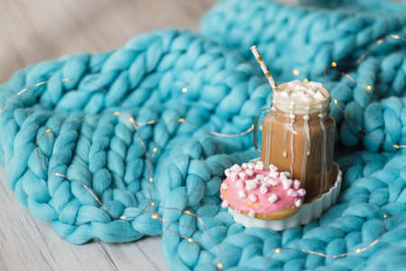 Pink donut with marshmallow and hot chocolate in cup on blue merino knit blanket.の写真素材
