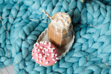Pink donut with marshmallow and hot chocolate in cup on blue merino knit blanket. Lights on backgroundの写真素材