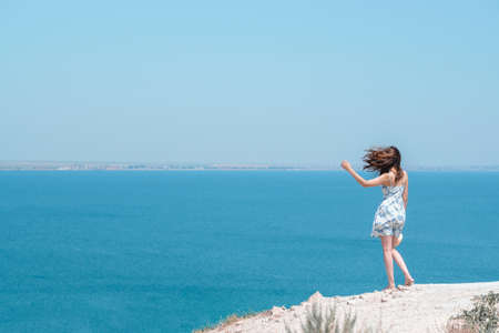 Caucasian woman stands on mountain and looks at the sea. Hair fluttering from the wind. Freedom Travel Concept Copyspaceの写真素材