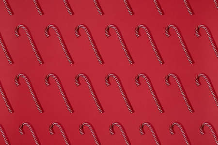 Striped red and white candy canes on red background. Cristmas lollipop. Trendy pattern Flat lay hard lightの写真素材