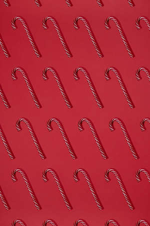 Striped red and white candy canes on red background. Cristmas lollipop. Trendy pattern Flat lay hard lightの写真素材