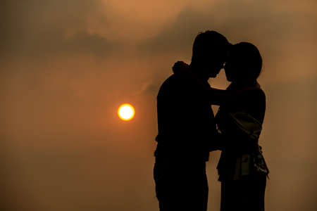 A light kiss,Romantic lovers hugging at twlilight with sunset in backgroundの写真素材