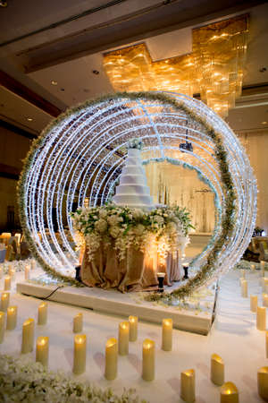 Flowers and decorations around wedding cake with chandelier on ceiling in the grand ballroom luxury hotel.のeditorial素材