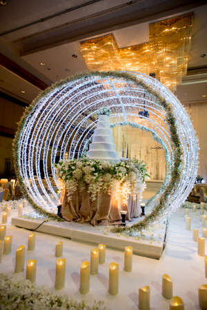 Flowers and decorations around wedding cake with chandelier on ceiling in the grand ballroom luxury hotel.のeditorial素材