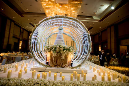 Flowers and decorations around wedding cake with chandelier on ceiling in the grand ballroom luxury hotel.のeditorial素材