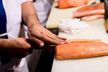 Cutting the salmon with a knife,Japanese chef making sashimi in kitchen,Sushi are madeの写真素材