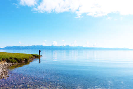 Man standing beside pure lake with blue sky.の写真素材
