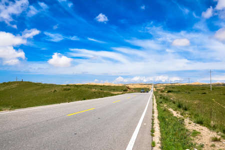Road on grassland with sunny blue sky and white cloudsの写真素材