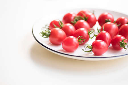 Fresh red cherry tomatoes  on a white plate on whiteの写真素材