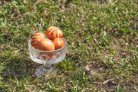 Some Easter eggs in crystal vase on a green lawn. Chicken eggs, natural color with lines. Day light, object on the right side of shot. Sunny day.の写真素材