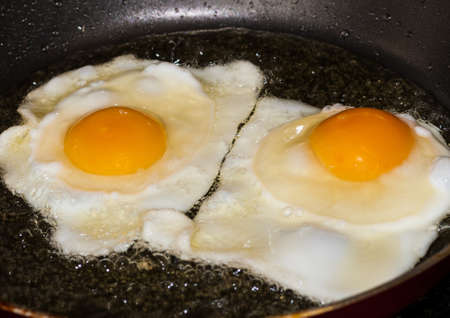 A pair of fried eggs cooking in a frying pan の写真素材