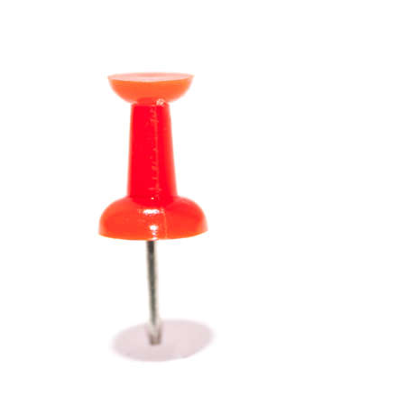 A macro shot of a single red push pin standing upright in a piece of white paper 
