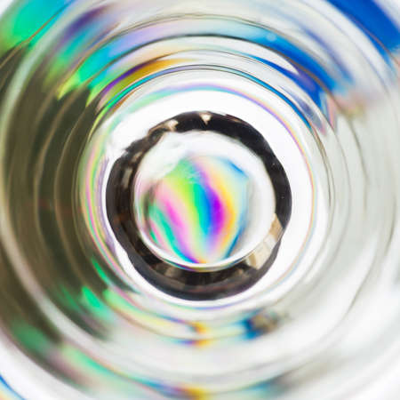 An abstract macro image depicting looking down through a shot glass to a colourful coaster 