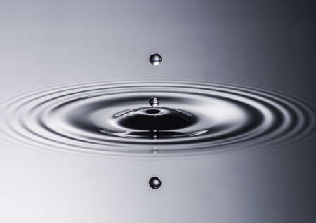 A macro shot of two water drops falling into a pool of water の写真素材