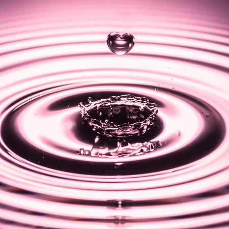 A water drop, in the shape of a heart, falls towards a splash made in a pool of water の写真素材