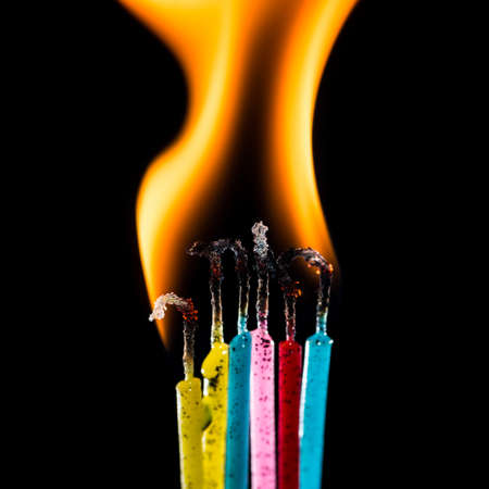 A macro shot of a group of colourful candles burning against a black background の写真素材