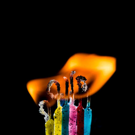 A macro shot of a group of colourful candles burning against a black background 