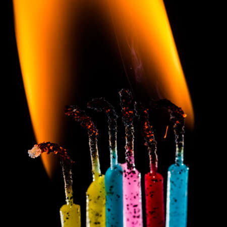 A macro shot of a group of colourful candles burning against a black background.の写真素材