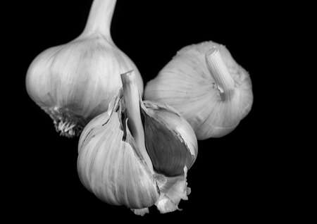 A black and white macro of a trio of garlic bulbs shot aganst a black background.