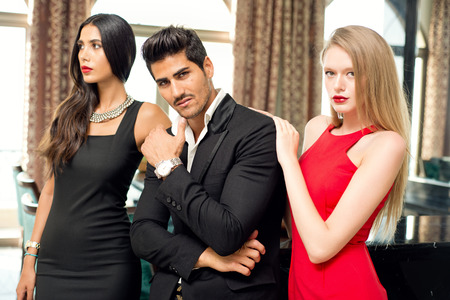 Portrait of a handsome fashionable man with two charming women posingの写真素材