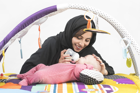 Arabian Mother feeding her baby girl on a play mat の写真素材
