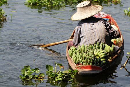 Farmer working sailing on small boat for selling organic fresh banana at river of floating market in Thailandの写真素材