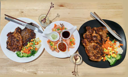 Homemade Dinner table serving with Sliced Grilled beef Ribeye steak and a slided raw salmon dressing with corn carrot peas lemon serving on white plate on wood table, dating night couple lover familyの写真素材