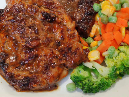 Sliced Grilled organic pork, beef Ribeye steak decorated with various colorful vegetables dressing corn carrot peas lemon serving on white plate on wooden table, One famous menu of secret recipe fromの写真素材