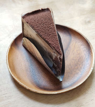 a slice of chocolate cake serving with cocoa powder on circle brown ceramic tray on dark brown table at coffee gourmet cafe, graphic design component, rough texture backgroundsの写真素材
