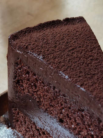 a slice of chocolate cake serving with cocoa powder on circle brown ceramic tray on dark brown table at coffee gourmet cafe, graphic design component, rough texture backgroundsの写真素材